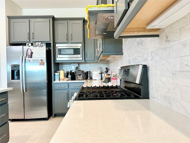 kitchen with light tile patterned floors, tasteful backsplash, gray cabinetry, appliances with stainless steel finishes, and exhaust hood