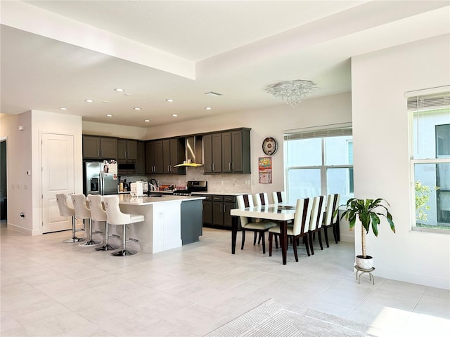 kitchen with plenty of natural light, wall chimney exhaust hood, stainless steel appliances, and decorative backsplash