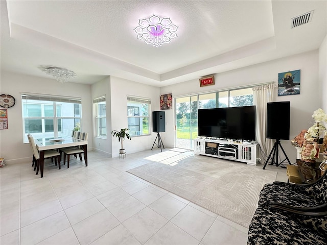 living area featuring a tray ceiling, visible vents, baseboards, and light tile patterned flooring