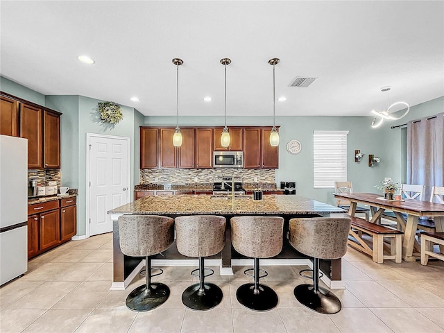 kitchen with hanging light fixtures, decorative backsplash, light stone countertops, and white refrigerator