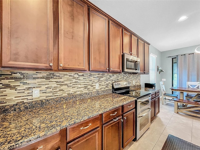 kitchen with backsplash, stainless steel appliances, light tile patterned flooring, and dark stone counters