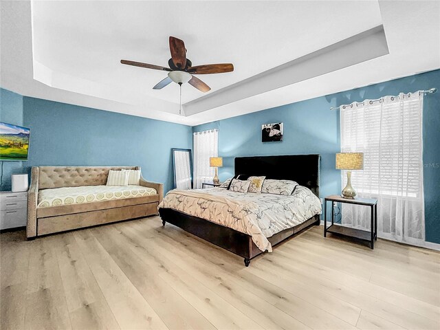 bedroom with light hardwood / wood-style floors, a raised ceiling, and ceiling fan