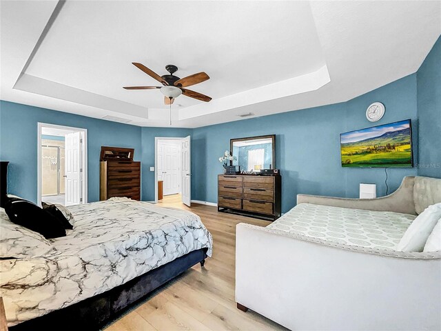 bedroom featuring light hardwood / wood-style floors, ceiling fan, and a raised ceiling