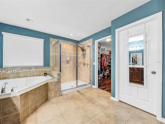 full bathroom featuring a textured ceiling, tile patterned flooring, a garden tub, a shower stall, and a walk in closet