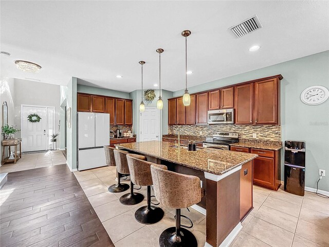 kitchen featuring backsplash, stainless steel appliances, a center island with sink, a breakfast bar area, and hanging light fixtures