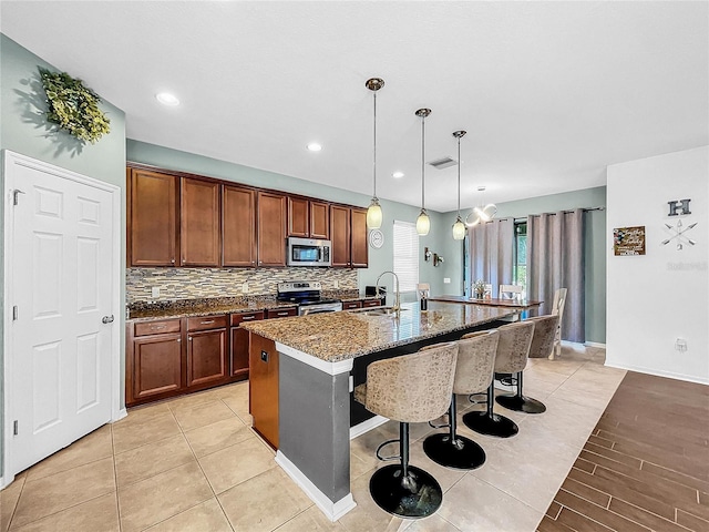 kitchen with backsplash, a kitchen island with sink, a kitchen bar, decorative light fixtures, and stainless steel appliances