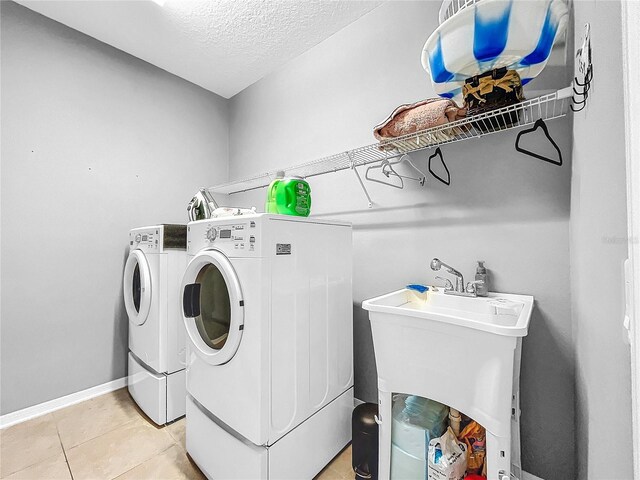 clothes washing area featuring sink, a textured ceiling, light tile patterned floors, and separate washer and dryer