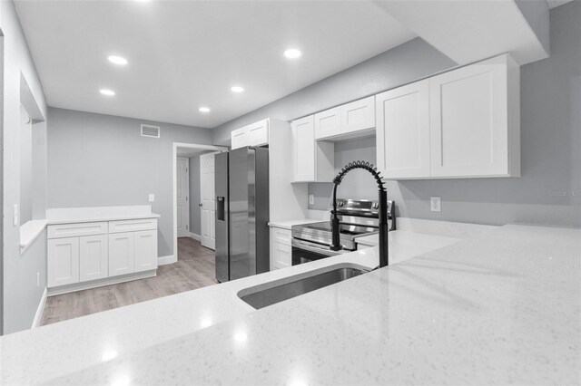 kitchen featuring appliances with stainless steel finishes, light hardwood / wood-style flooring, white cabinetry, and light stone counters