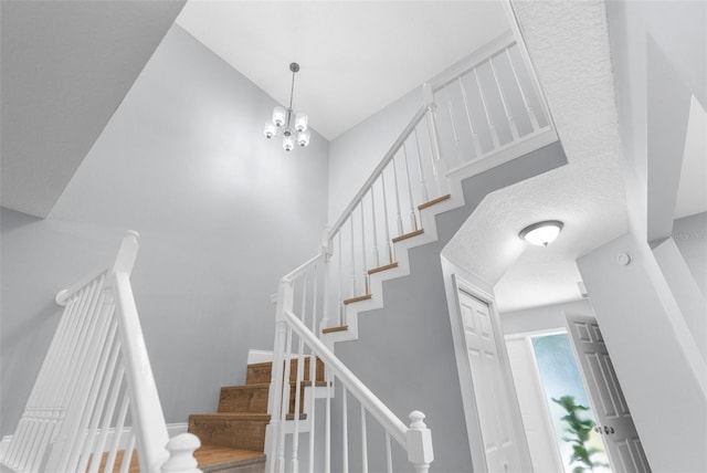 staircase featuring a textured ceiling, an inviting chandelier, and a high ceiling