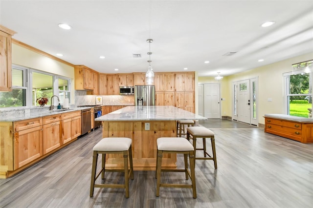 kitchen with light stone countertops, stainless steel appliances, decorative light fixtures, light hardwood / wood-style floors, and a kitchen island