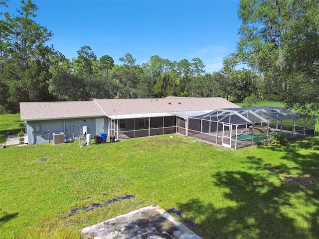 back of property with a lawn, glass enclosure, central AC, and a pool