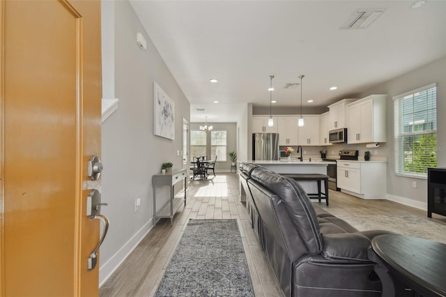 living room with sink, a notable chandelier, and light hardwood / wood-style flooring