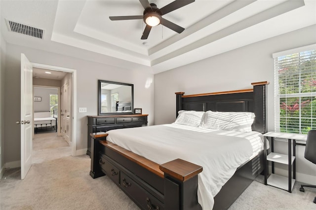 carpeted bedroom featuring a tray ceiling, multiple windows, and ceiling fan