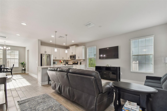 living room featuring light wood-type flooring, a wealth of natural light, an inviting chandelier, and sink