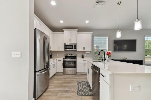 kitchen featuring pendant lighting, stainless steel appliances, sink, white cabinets, and light hardwood / wood-style floors