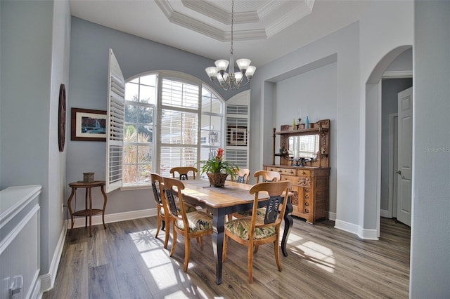 dining room featuring arched walkways, wood finished floors, baseboards, ornamental molding, and a raised ceiling