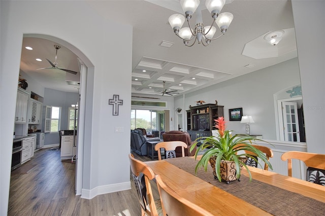 dining area with arched walkways, coffered ceiling, wood finished floors, and ceiling fan with notable chandelier