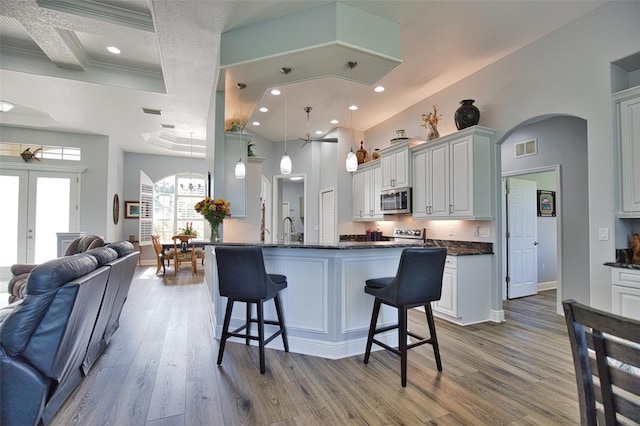 kitchen with a breakfast bar, stainless steel microwave, visible vents, open floor plan, and wood finished floors