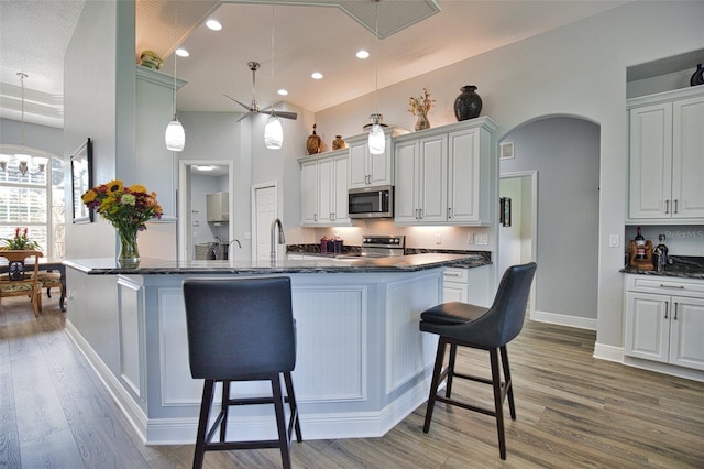 kitchen featuring arched walkways, light wood-style flooring, a kitchen breakfast bar, hanging light fixtures, and appliances with stainless steel finishes