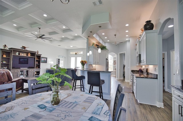 dining room featuring arched walkways, visible vents, ceiling fan, light wood-type flooring, and coffered ceiling