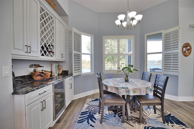 dining room with beverage cooler, baseboards, a bar, and wood finished floors