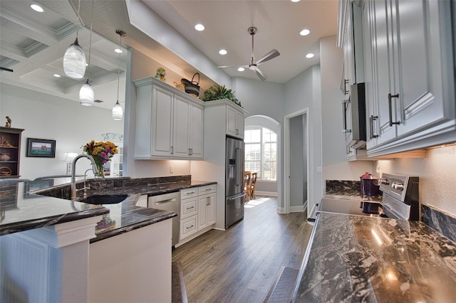 kitchen with arched walkways, stainless steel appliances, a sink, wood finished floors, and coffered ceiling