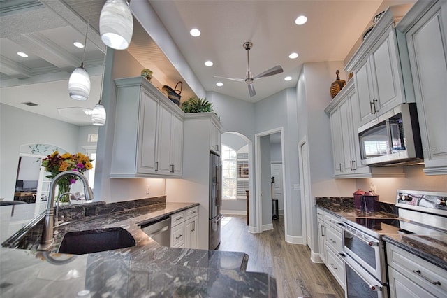 kitchen featuring arched walkways, stainless steel appliances, light wood-style floors, a sink, and dark stone countertops