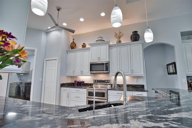 kitchen featuring arched walkways, hanging light fixtures, appliances with stainless steel finishes, washing machine and dryer, and dark stone counters