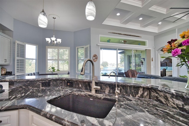 kitchen featuring coffered ceiling, dark stone countertops, beamed ceiling, a sink, and a notable chandelier