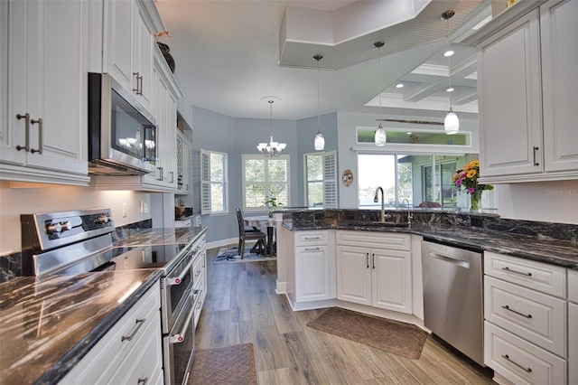 kitchen featuring appliances with stainless steel finishes, white cabinetry, a sink, light wood-type flooring, and a peninsula