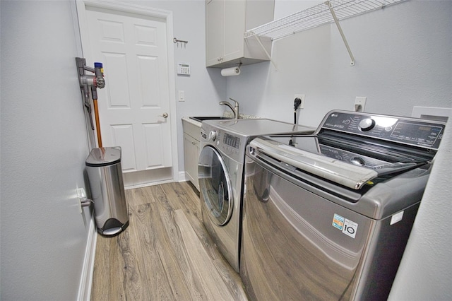 clothes washing area with cabinet space, a sink, light wood-type flooring, independent washer and dryer, and baseboards