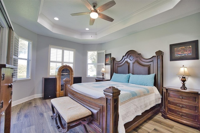 bedroom featuring a tray ceiling, crown molding, recessed lighting, wood finished floors, and baseboards