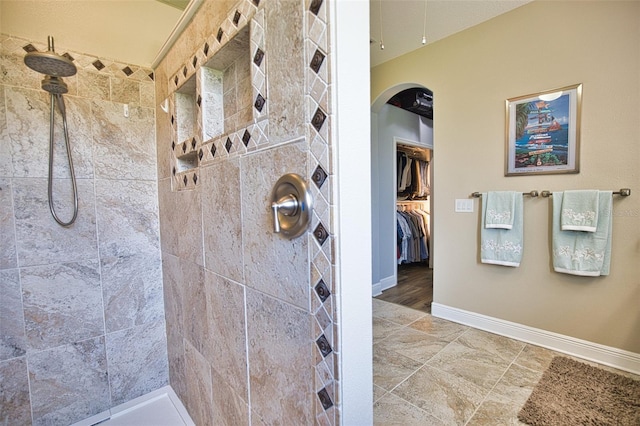 bathroom with a tile shower and baseboards