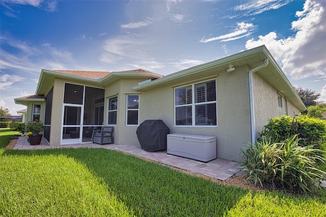 back of property featuring a sunroom, a patio area, a yard, and stucco siding