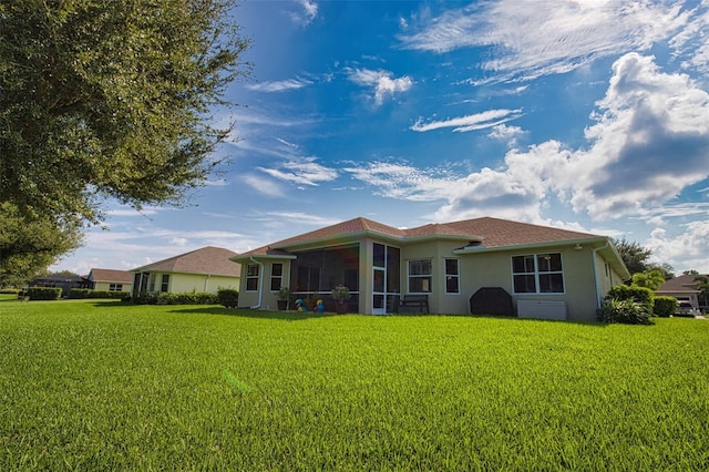 back of property with a sunroom, stucco siding, and a yard