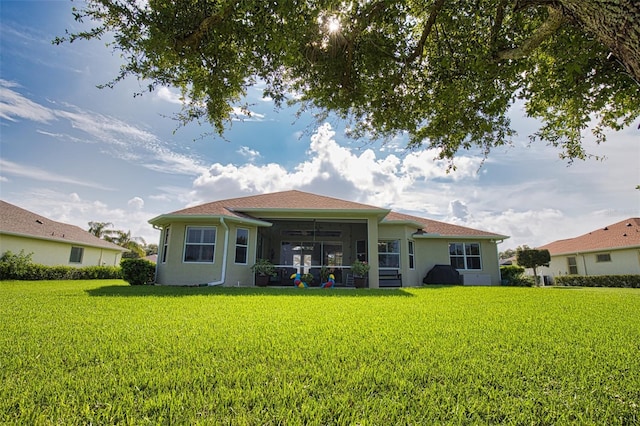 back of property featuring a sunroom, a lawn, and stucco siding