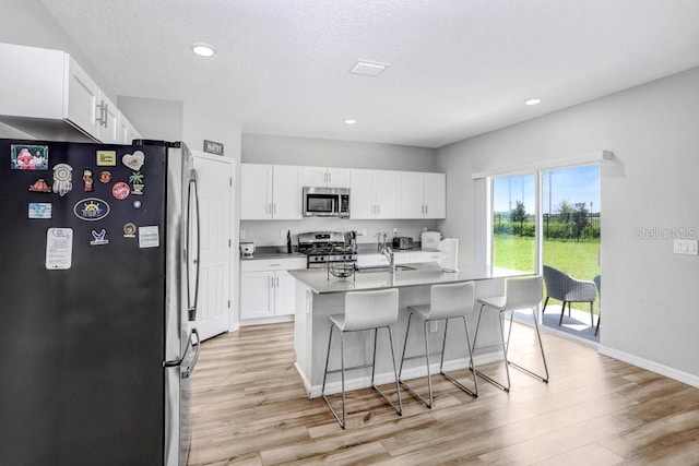 kitchen with light wood-type flooring, a kitchen island with sink, stainless steel appliances, and white cabinetry