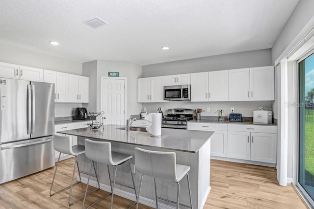 kitchen featuring appliances with stainless steel finishes, light hardwood / wood-style flooring, white cabinets, and an island with sink