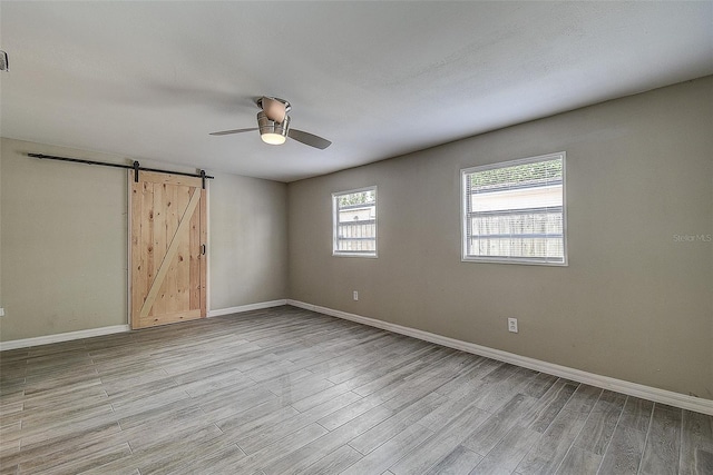 unfurnished room featuring ceiling fan, light wood-type flooring, and a barn door