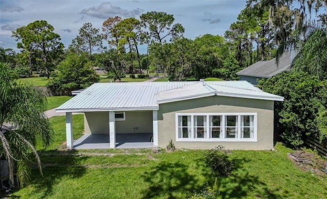 rear view of house featuring stucco siding, metal roof, a lawn, and a patio