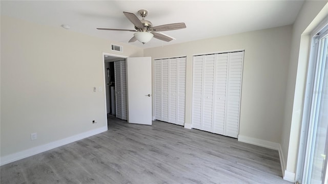 unfurnished bedroom featuring ceiling fan, light wood-type flooring, and multiple closets