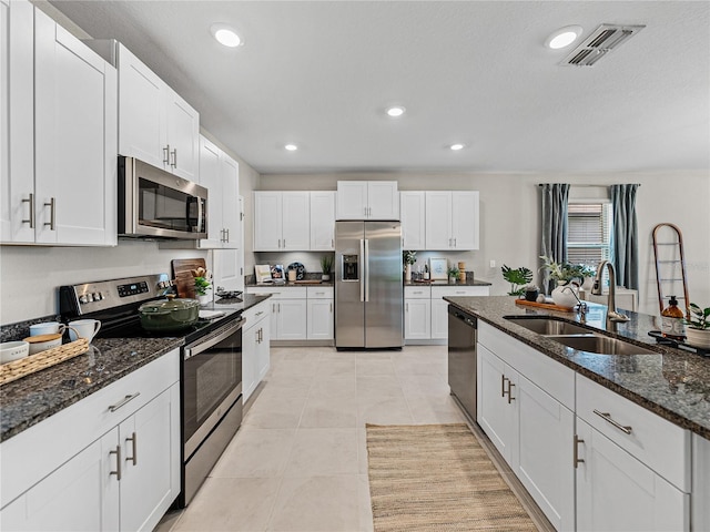 kitchen with light tile patterned floors, sink, white cabinetry, appliances with stainless steel finishes, and dark stone countertops