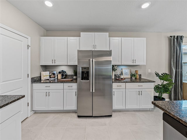 kitchen with dark stone countertops, light tile patterned flooring, stainless steel appliances, and white cabinets