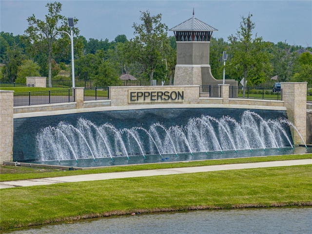 community / neighborhood sign featuring a lawn and a water view