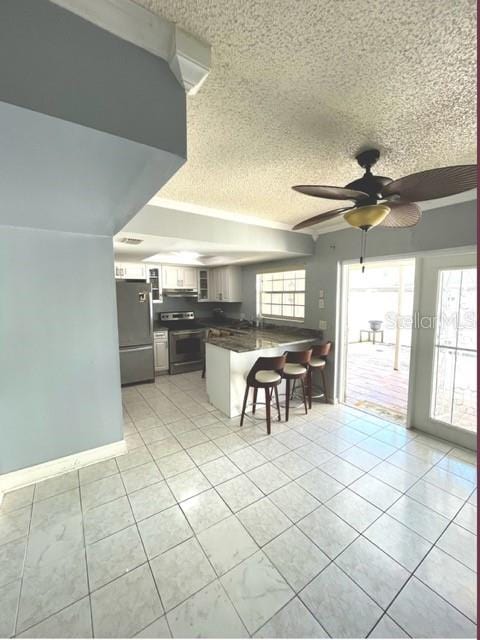 kitchen featuring appliances with stainless steel finishes, a kitchen bar, white cabinets, kitchen peninsula, and ceiling fan