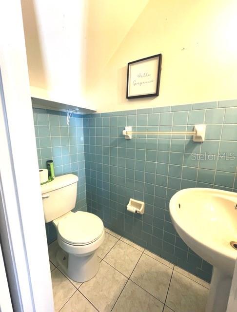 bathroom featuring tile patterned flooring, tile walls, toilet, and sink