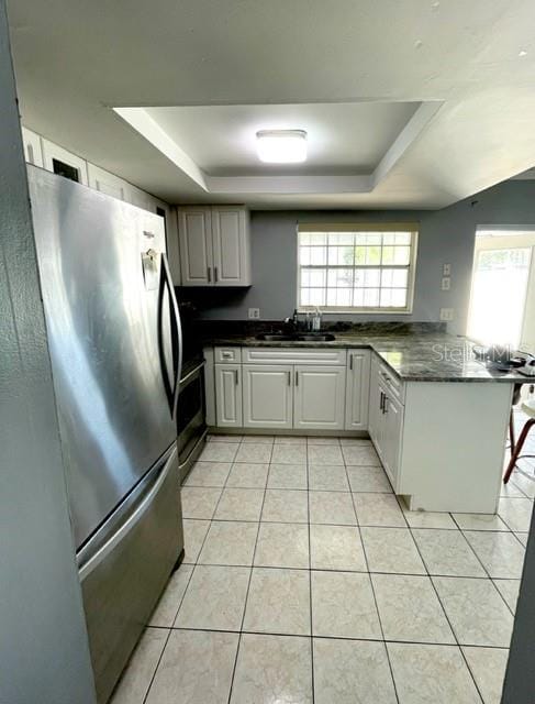 kitchen with sink, stainless steel refrigerator, kitchen peninsula, and a tray ceiling