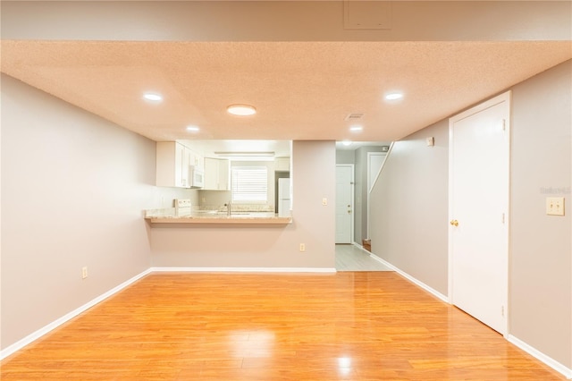 unfurnished living room featuring a textured ceiling, light hardwood / wood-style flooring, and sink