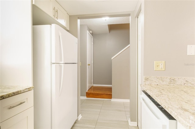 kitchen with light wood-type flooring, white cabinets, white appliances, and light stone countertops