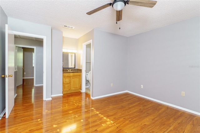 unfurnished bedroom with wood-type flooring, connected bathroom, a textured ceiling, and ceiling fan